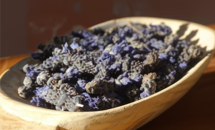 A wooden bowl filled with dried lavender buds, bathed in warm light.